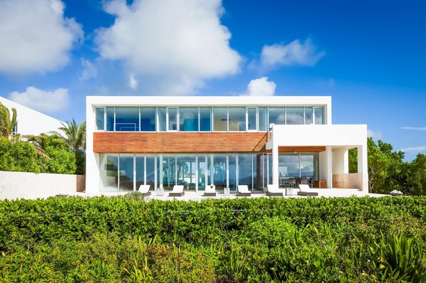 A modern two-story house with large glass windows and a wooden deck. - Beaches Edge | Oceanfront Estate, Anguilla (Blowing Point Village)