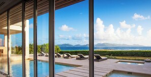 A modern pool area with lounge chairs and a view of the ocean and mountains. - Beaches Edge | Oceanfront Estate, Anguilla (Blowing Point Village)