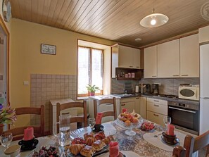 A dining area with a table set for two, a kitchen with basic appliances, and a window with curtains.