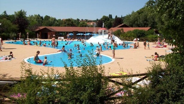 A public swimming pool with multiple lanes, surrounded by a sandy beach area and shaded by trees.
