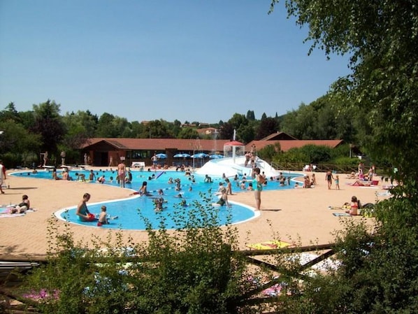 A swimming pool area with multiple pools, a sandy beach, and a building in the background.