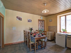 Uma sala de jantar com mesa e cadeiras de madeira, um relógio na parede e uma janela com vista.