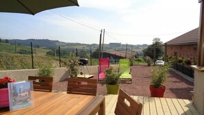 An outdoor patio with a wooden table and chairs, potted plants, and a view of the countryside.