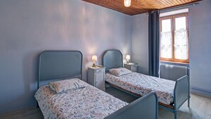 A room with two beds, a wooden ceiling, a window with curtains, and a radiator.