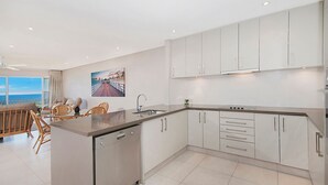 A modern kitchen with white cabinets, a built-in dishwasher, and a large window overlooking a scenic view. - Quarterdeck 20 - Spectacular Ocean Views (Lennox Head)
