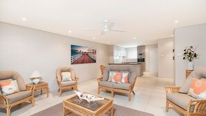 A spacious living room with wicker furniture, a glass coffee table, and a painting of a pier. - Quarterdeck 20 - Spectacular Ocean Views (Lennox Head)