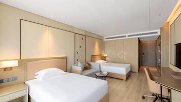 Ein Hotelzimmer mit zwei Betten, einem Schreibtisch, einem Sessel und einem Fernseher.