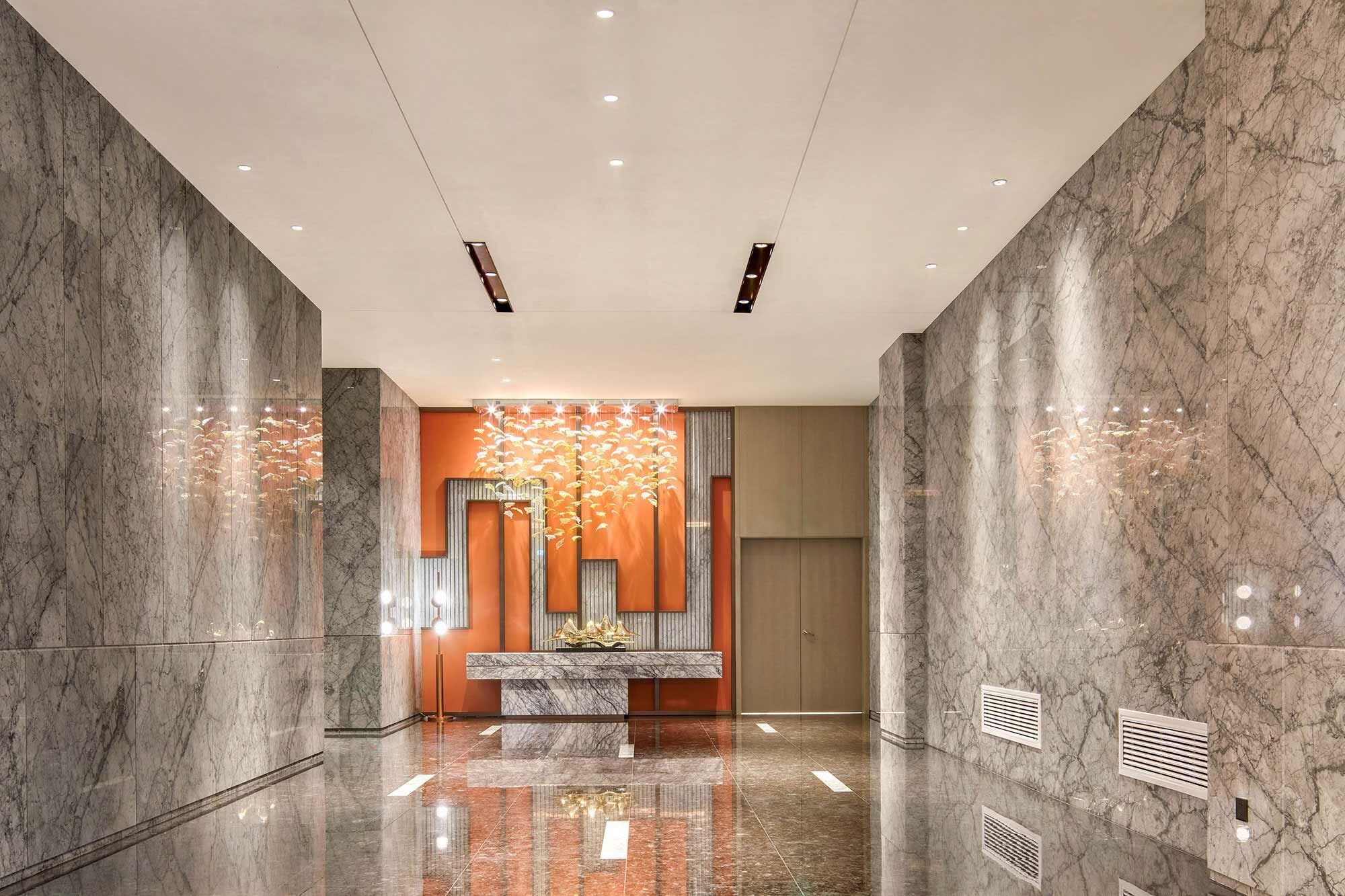 Un lobby moderno con paredes de mármol, una recepción y un elemento decorativo de iluminación.