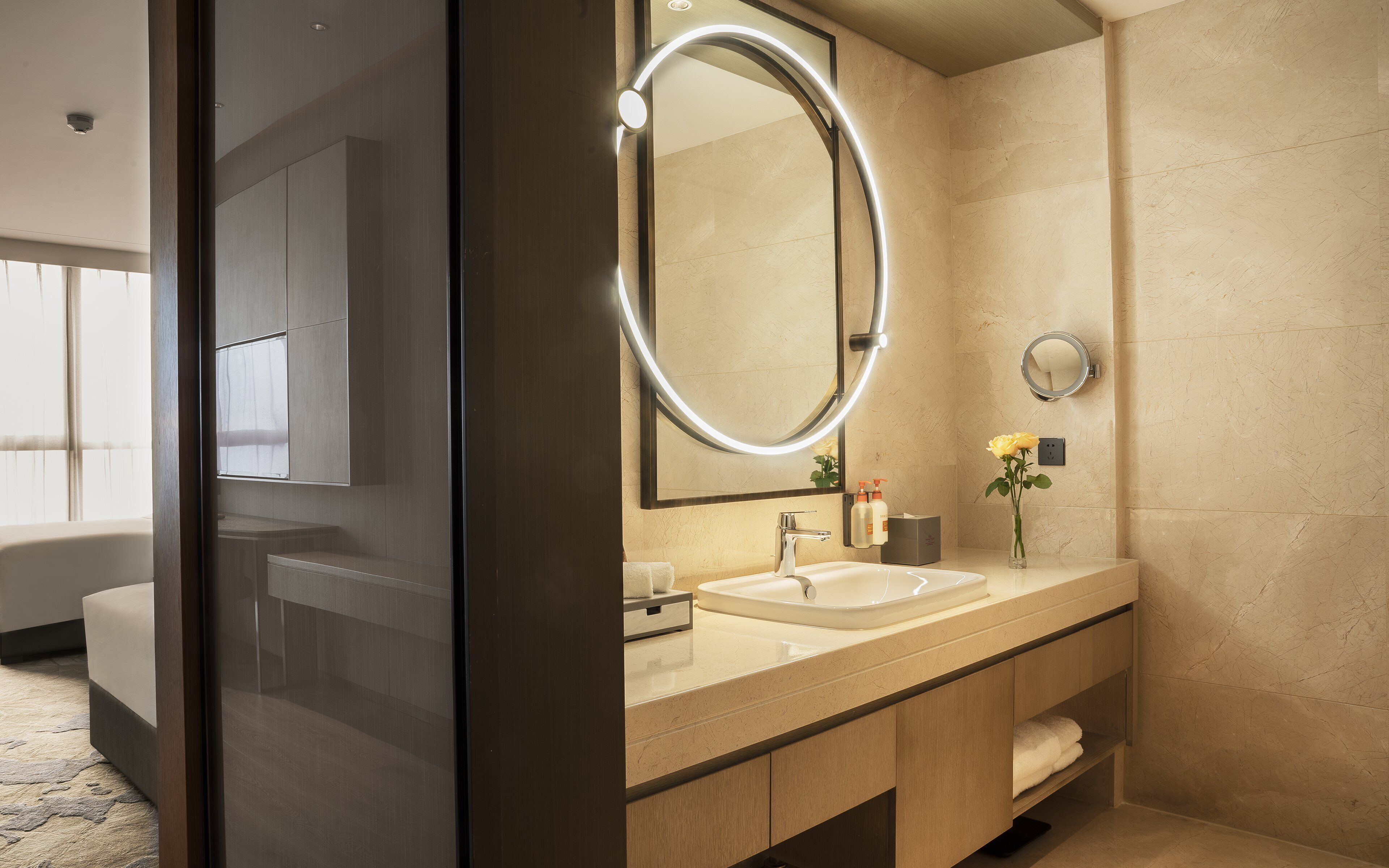 A modern bathroom with a large mirror, a sink, and a vase with a yellow flower.
