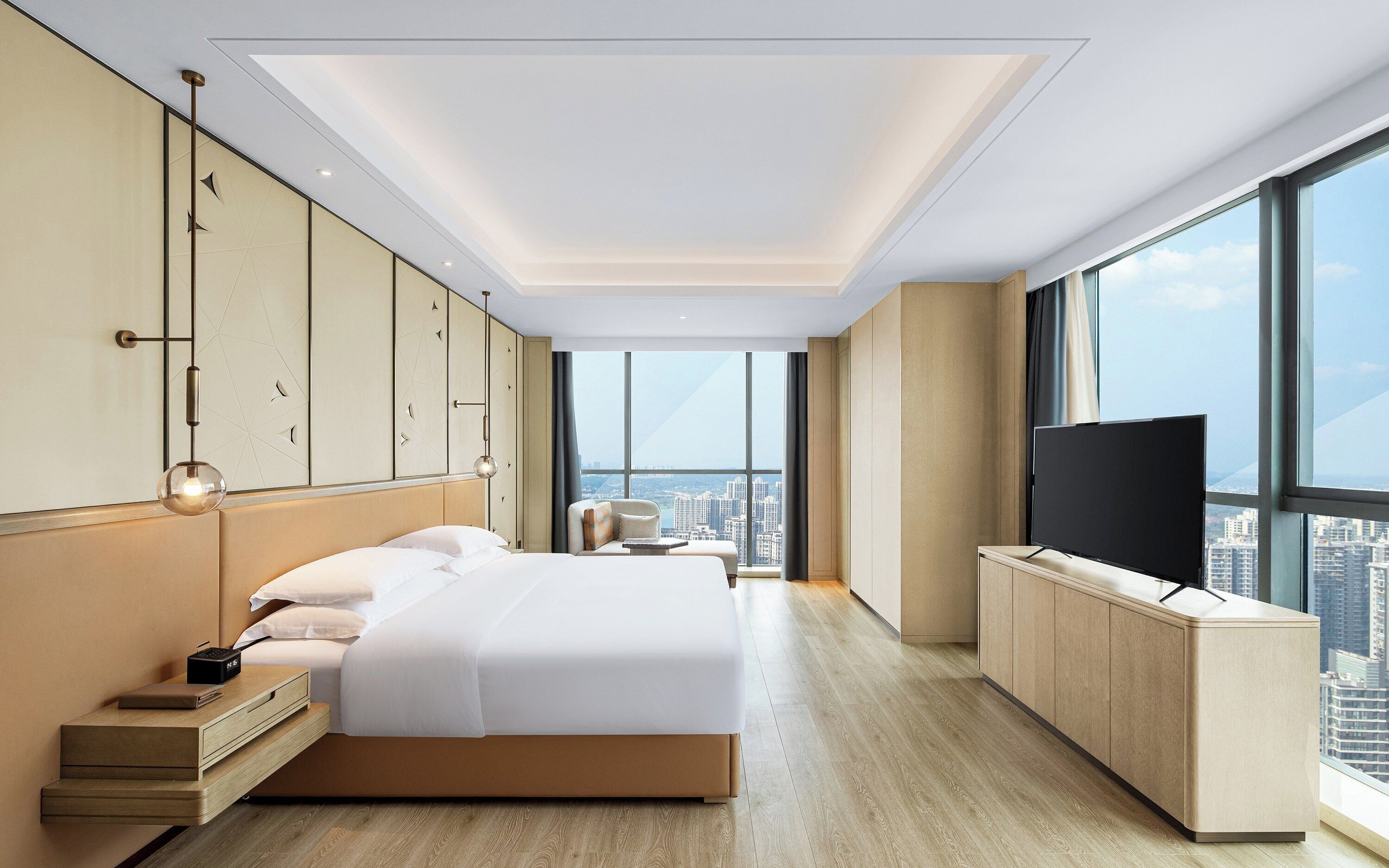 A modern hotel room with a large bed, a desk, a TV, and a city view.