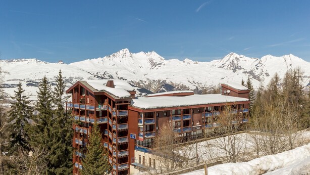 Un hôtel à plusieurs étages, doté de balcons et entouré de montagnes enneigées.