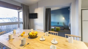 Une chambre d’hôtel dotée d’un coin repas avec une table en bois, dressée avec des fruits, des tasses et un téléviseur fixé au mur.