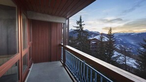 Un balcon en bois, doté d’une rambarde en métal, qui offre une vue sur un paysage montagneux.