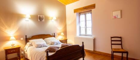 A bedroom with a wooden bed, bedside lamps, a window with curtains, and a chair.