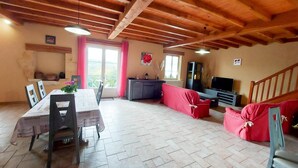 A spacious living area with a wooden ceiling, a dining table with chairs, a red sofa, a TV, and a staircase.