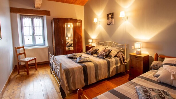 A bedroom with a wooden ceiling, a bed with a striped bedspread, a chair, a wardrobe, and two bedside lamps.