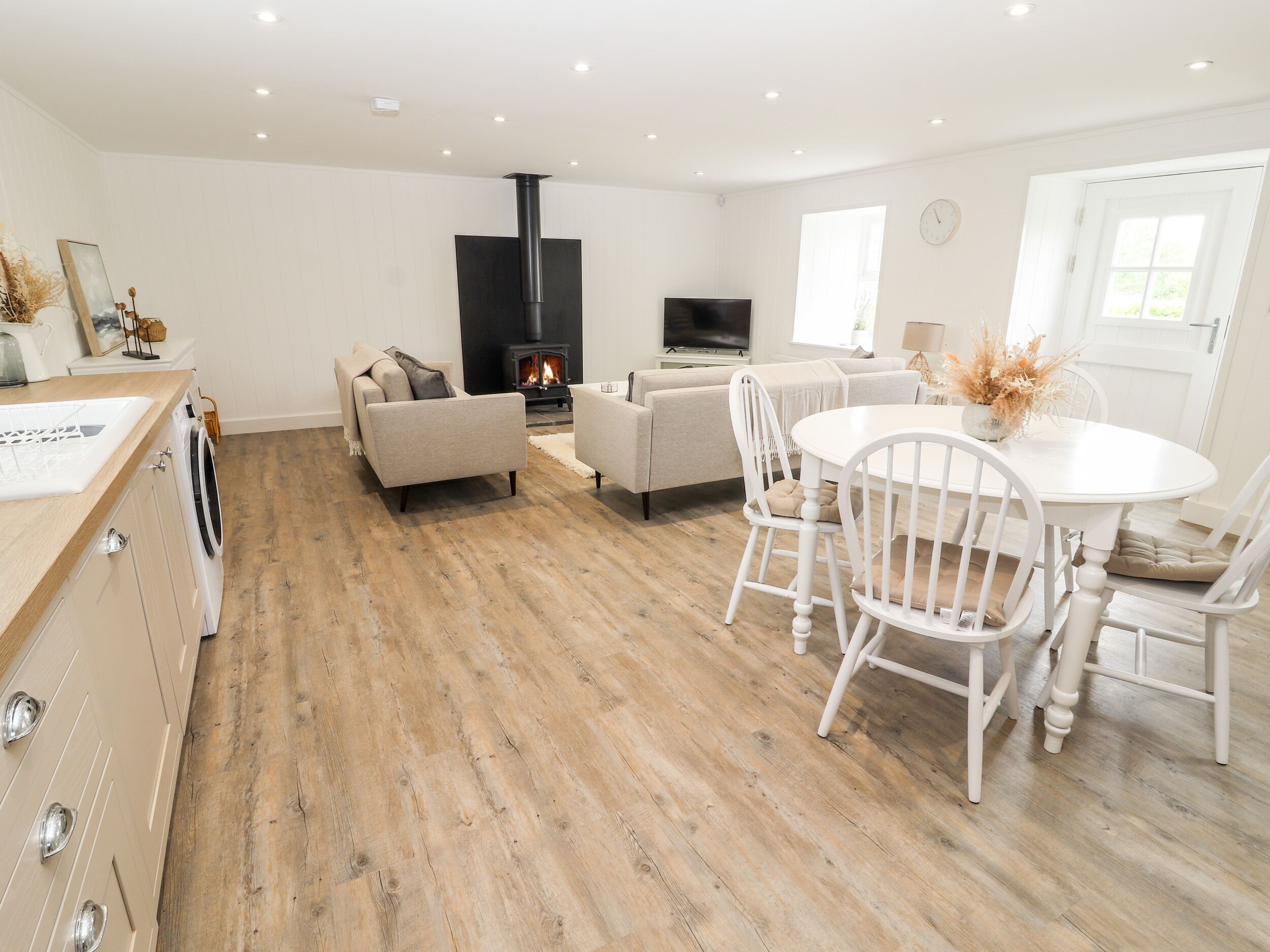 A spacious living room with a fireplace, sofas, a dining table, and a kitchen area with a washing machine.
