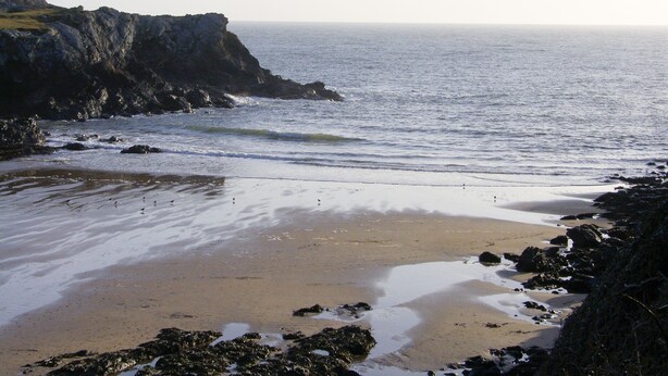 A coastal beach with rocky cliffs and calm waves.