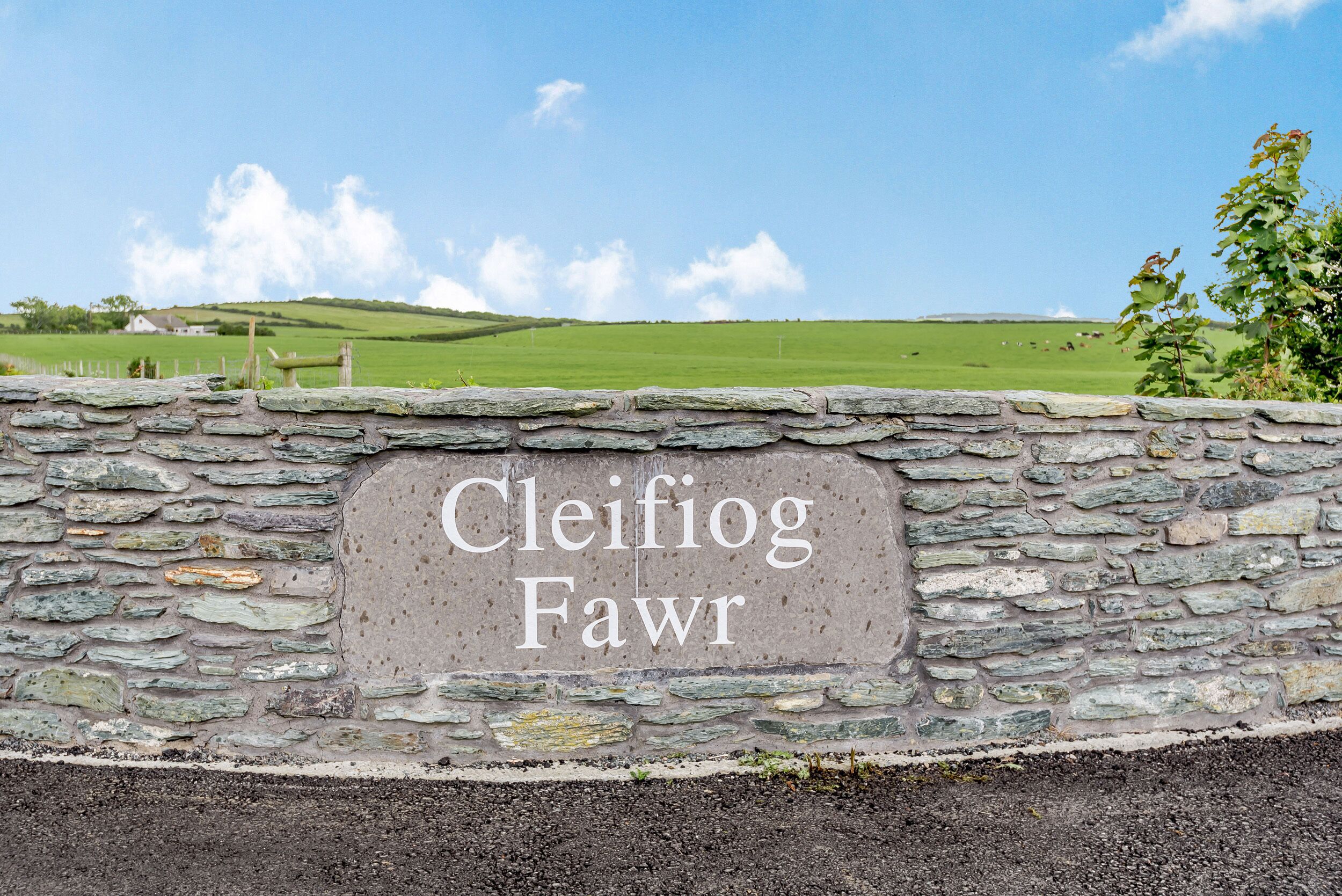 A stone wall with the inscription "Cleifiog Fawr" and a view of green fields in the background.