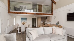 A spacious living area with a large sofa, a dining table, and a kitchen in the background. - Sgubor (Holyhead)