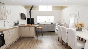 A modern kitchen with wooden flooring, a central island, and a dining area with chairs and a table. - Sgubor (Holyhead)