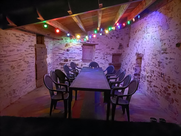 Un coin repas rustique avec une longue table et des chaises, des poutres en bois au plafond et des murs en pierre.