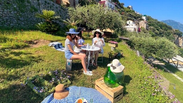 Un gruppo di persone che fa un picnic su un pendio erboso, con muri di pietra e edifici sullo sfondo.