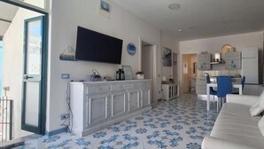 Un soggiorno moderno con un divano bianco, un angolo cottura con una sedia blu e un tavolo da pranzo.