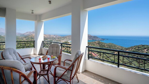 Un balcón con mobiliario de mimbre y una mesa, con vistas a un paisaje costero.