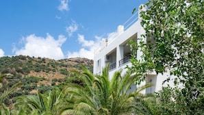 Un edificio blanco con balcones, rodeado de abundante vegetación y un cielo azul despejado.