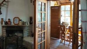 A rustic interior with a fireplace, wooden beams, a dining area, and a cross on the wall.