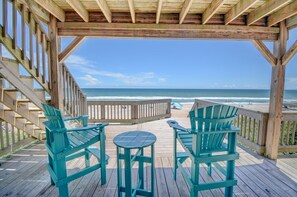 Une terrasse en bois avec deux chaises et une table, donnant sur une plage avec l’océan en arrière-plan.