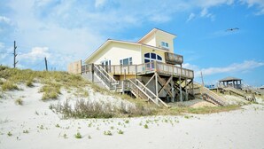 Ein Strandhaus mit Holzterrasse, mehreren Fenstern und einem Balkon.
