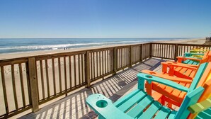 Eine Holzterrasse mit bunten Adirondack-Stühlen mit Blick auf einen Strand.