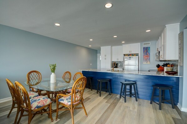 A modern kitchen with a blue countertop, white cabinets, and a dining area with wicker chairs and a glass table.