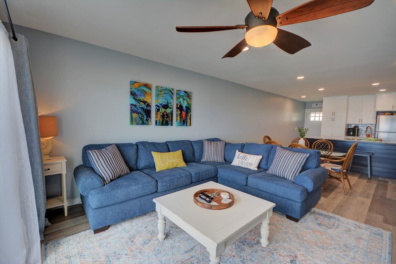 A modern living room with a blue sectional sofa, a white coffee table, and a ceiling fan.