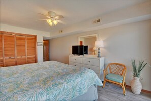 A bedroom with a bed, a dresser, a television, a ceiling fan, and a chair.