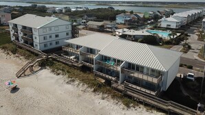 Un hotel costero con varias edificaciones, incluyendo una construcción principal de varios pisos con balcones y un edificio más pequeño con piscina.