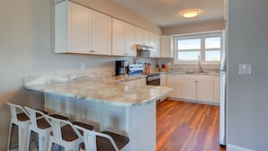 A modern kitchen with white cabinets, a marble countertop, and a built-in island with bar stools. - Oceanfront bliss awaits you at Cool Story, a 3BR retreat in North Topsail Beach. (North Topsail Beach)