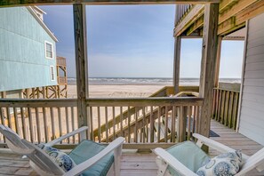 Een houten terras met twee loungestoelen en uitzicht op het strand.