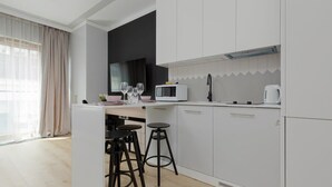 Une cuisine moderne avec des meubles blancs, un four à micro-ondes et une bouilloire. Il y a deux tabourets noirs autour d’une petite table.