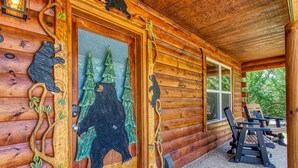 A log cabin with a wooden door featuring bear carvings and a glass panel with a bear and trees.