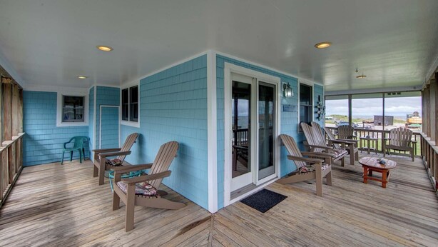 A covered porch with wooden flooring, blue walls, and several Adirondack chairs.