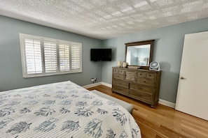 A bedroom with a bed, dresser, television, and a window with blinds.