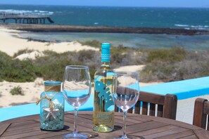 Een tafel met een fles wijn, twee glazen en een potje met een zeester. Op de achtergrond is een strand en uitzicht over de oceaan te zien.