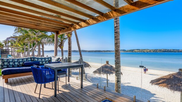A wooden deck with a pool, seating area, and a view of the beach.