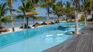 A pool area with clear blue water, surrounded by palm trees and a wooden deck.