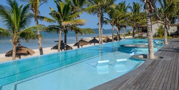 Un área de piscina con agua cristalina, rodeada de palmeras y una terraza de madera.
