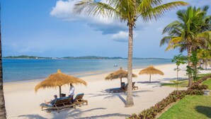 A beach with thatched umbrellas, lounge chairs, and palm trees.