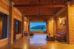 A covered outdoor area with stone walls, wooden benches, and a view of a landscape. - Wagoba Eco lodge (Bhadravathi)